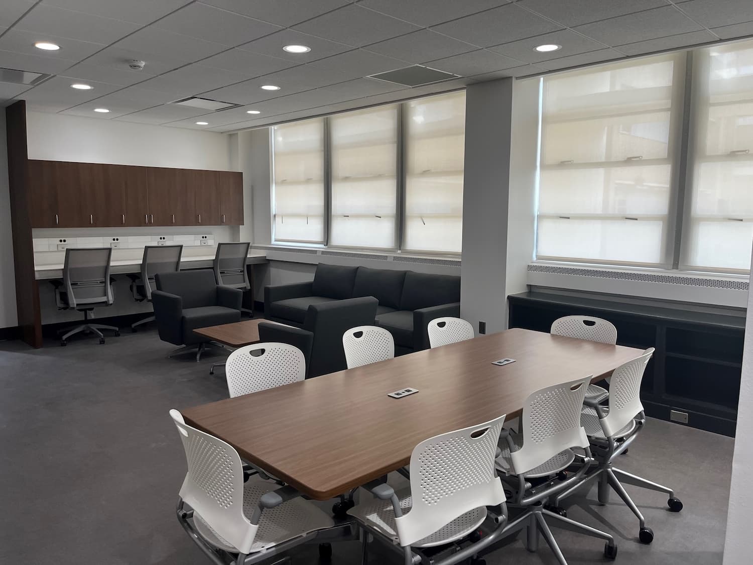 Residents' Lounge with wooden conference table and office chairs, lounge area with upholstered chairs, couch and small table, and study area with three office chairs and counter with electric outlets.